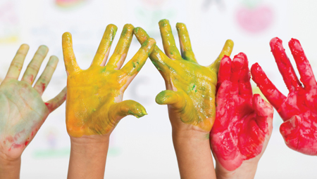 Cinco manos de niños cubiertas de pintura levantadas en el aire.