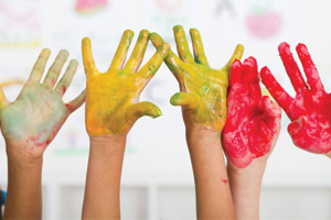 Five child hands covered in paint raised into the air.