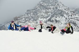 Five children at the top of a snow covered hill about to sled down