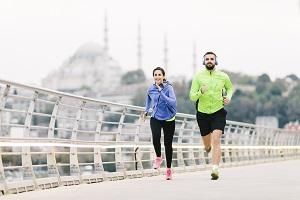 A woman and man in athletic attire jogging on a bridge in a city